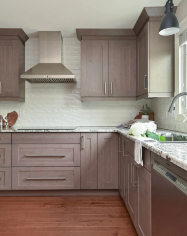 Modern kitchen with gray-brown cabinets, stainless steel range hood, granite countertops, and wood floors.