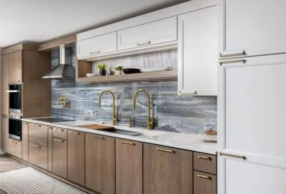 Modern kitchen with light and dark wood cabinets, gold fixtures, and a white countertop.