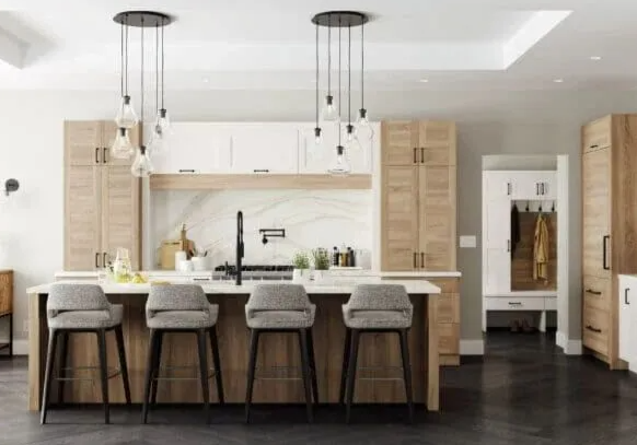 Kitchen with light wood cabinets, white countertops, four bar stools, and pendant lights.
