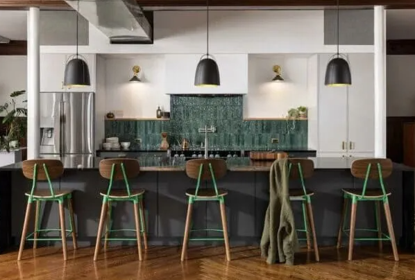 Modern kitchen with dark countertops, green-accented bar stools, and pendant lights over the island.