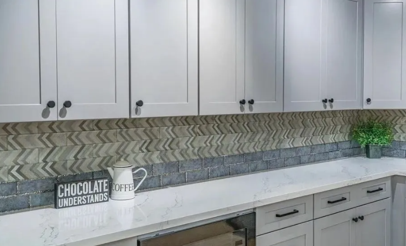 Kitchen with light gray cabinets, patterned backsplash, white countertops, and black hardware.