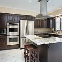 Dark wood kitchen with stainless steel appliances, white tile floor, and a granite island with stools.
