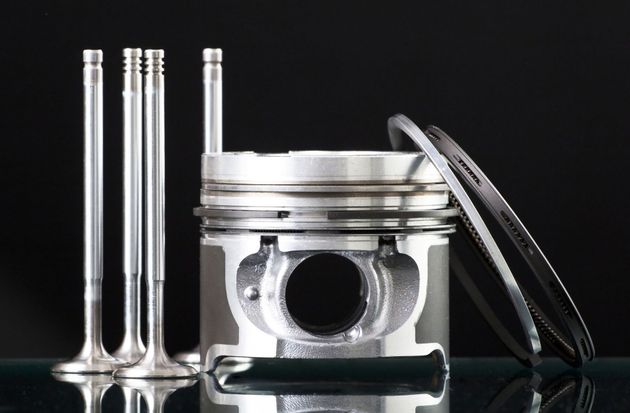 Silver engine piston with valves and a ring on a black reflective surface