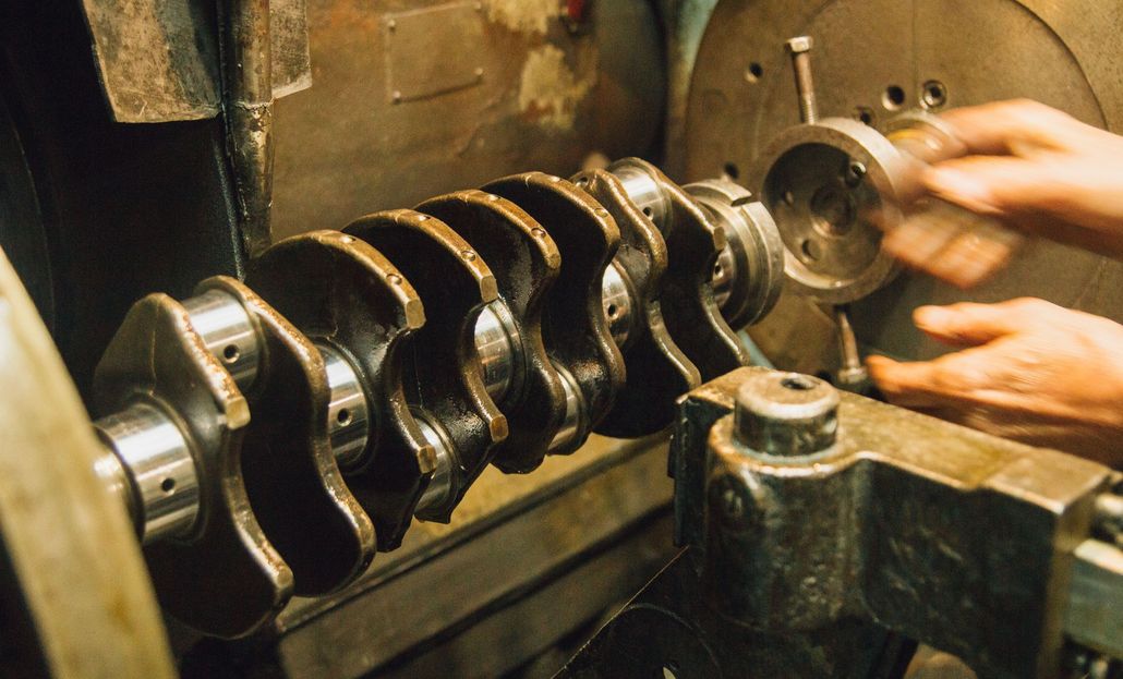 Close-up of hands polishing a metal crankshaft in a workshop machine.