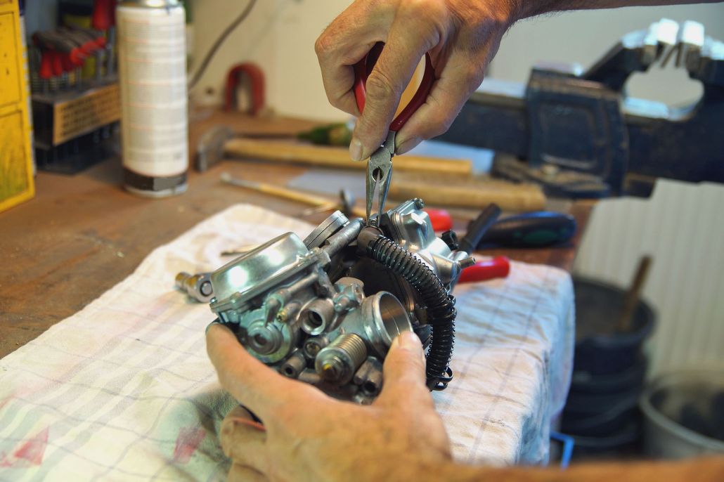 Hands repairing a mechanical engine on a workbench with tools and cloth underneath.