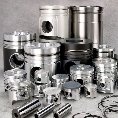 Assorted shiny metal engine pistons and parts arranged on a gray surface