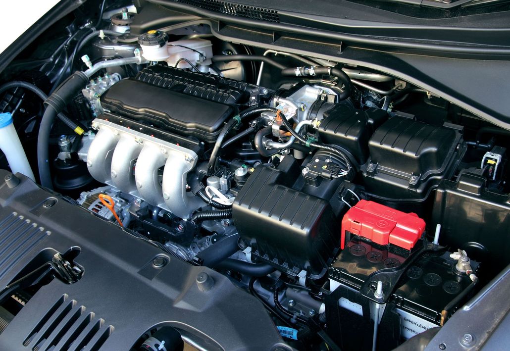Car engine bay with shiny black cover, silver intake manifold, and red battery terminal.