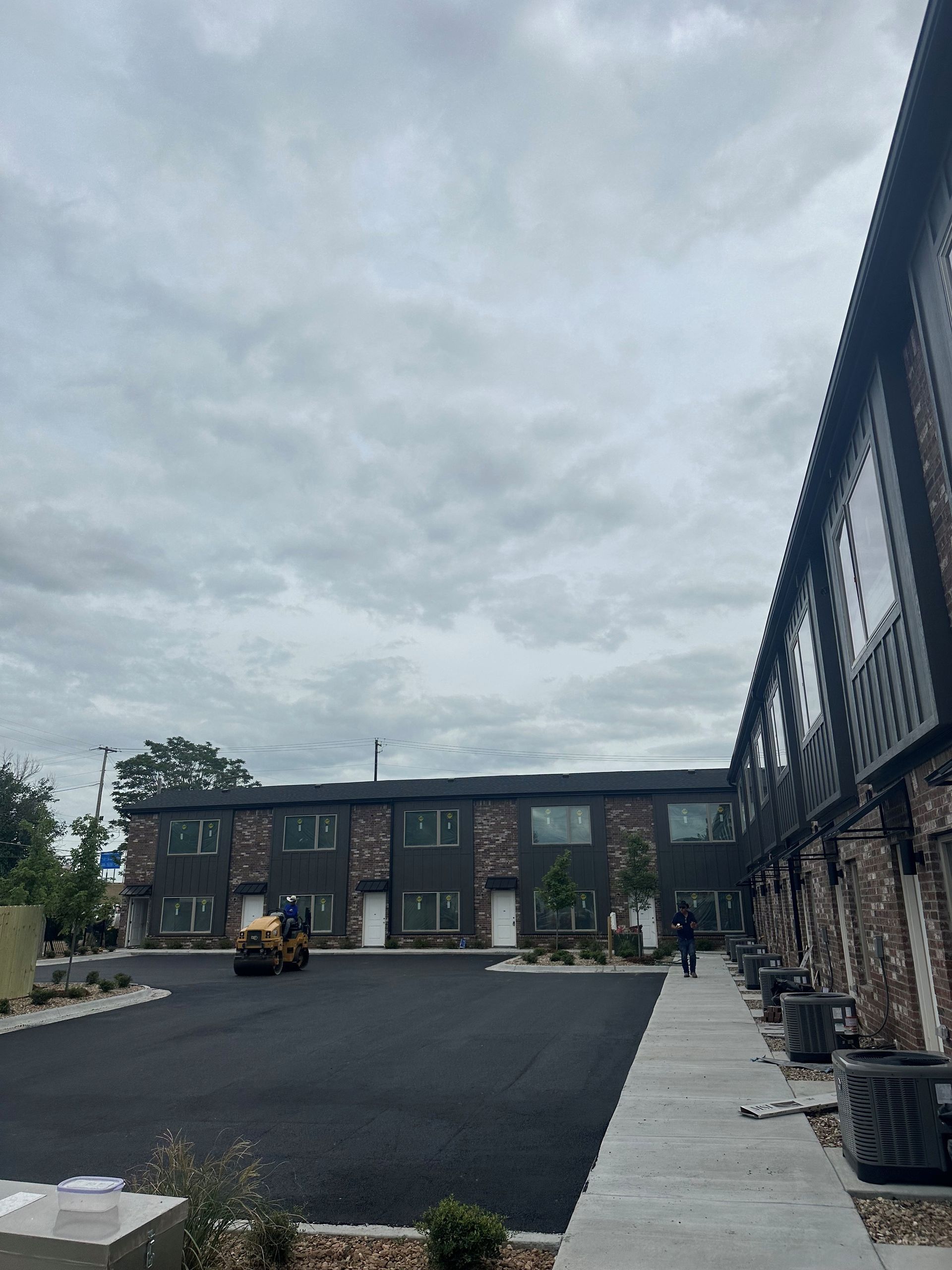 Apartment courtyard with a fresh blacktop parking lot, stone buildings, and cloudy sky.