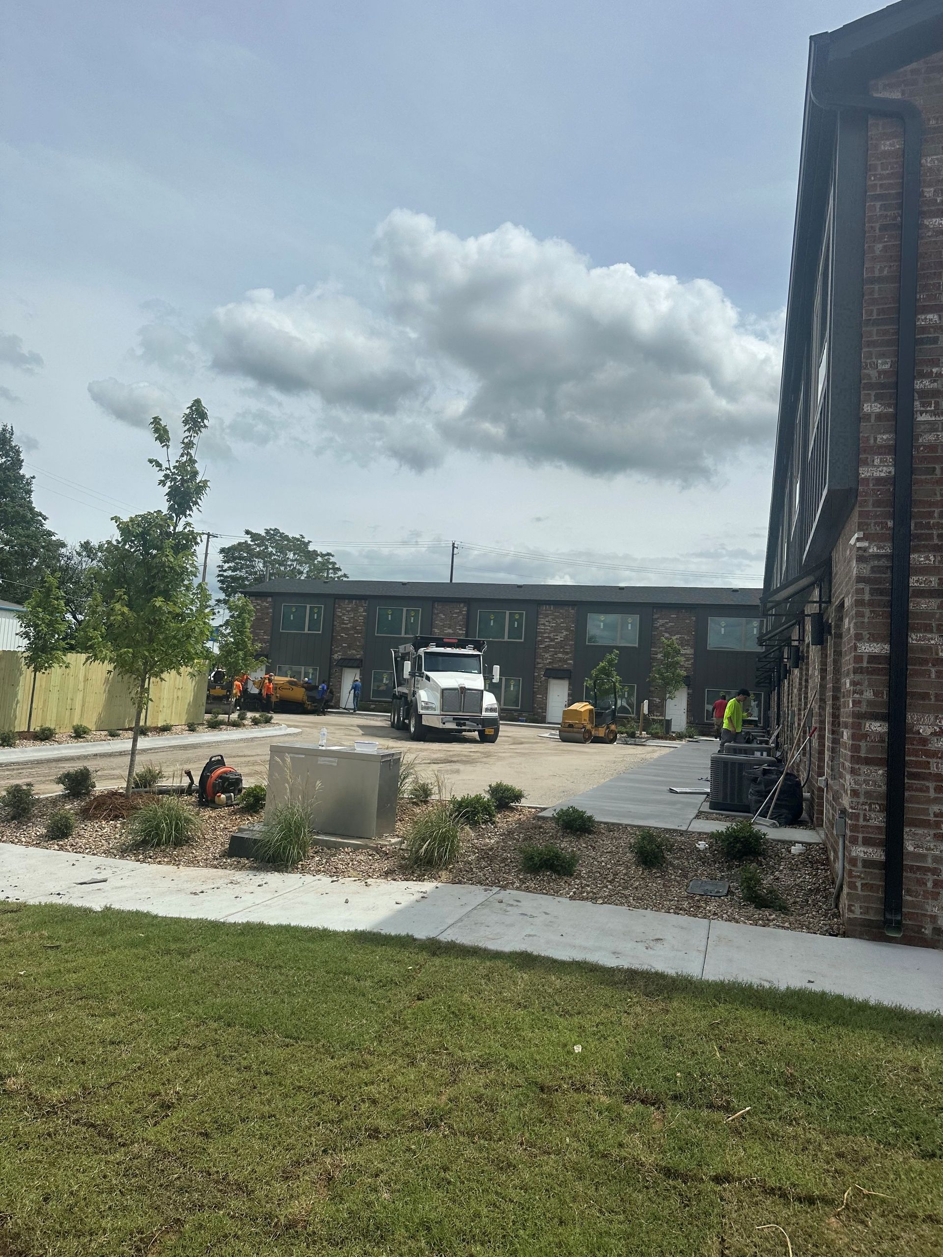 Modern building courtyard with a white vehicle, landscaped beds, and cloudy sky.