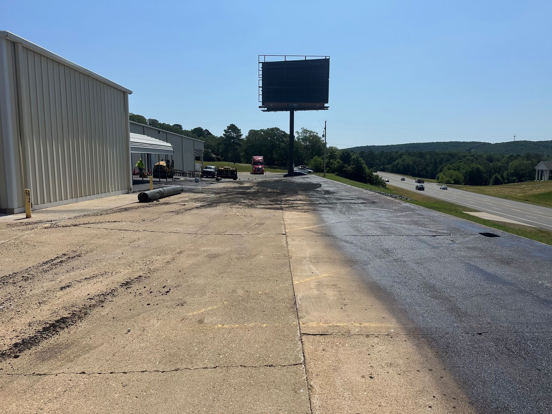 Roadside pull-off with a large blank sign, concrete barrier, and highway under a clear blue sky.