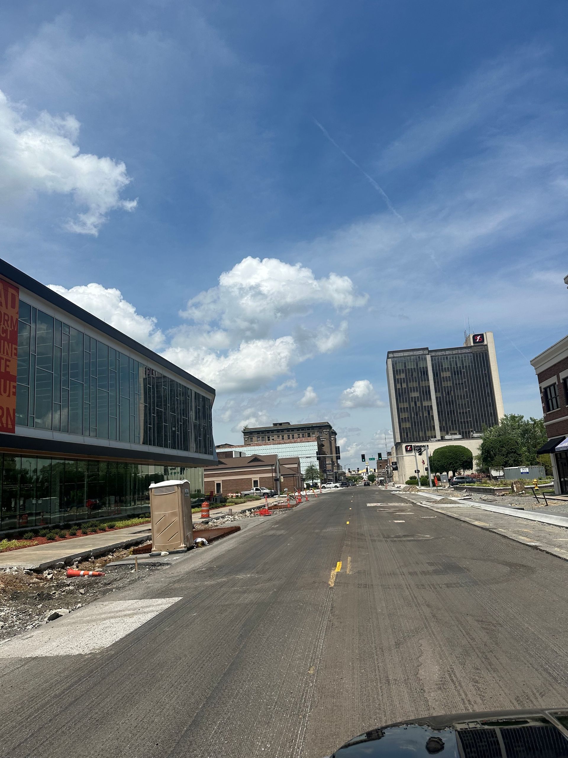Damaged roadway beside partially demolished buildings under a bright blue sky with clouds.
