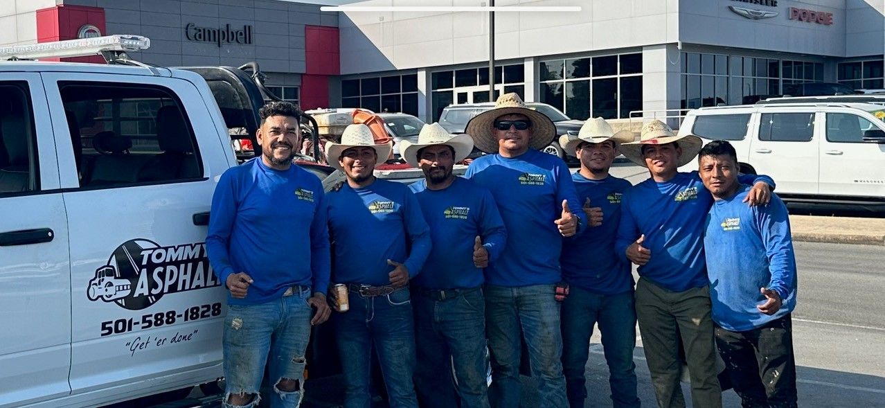 Group of workers in blue shirts posing beside a white service truck outside a building.