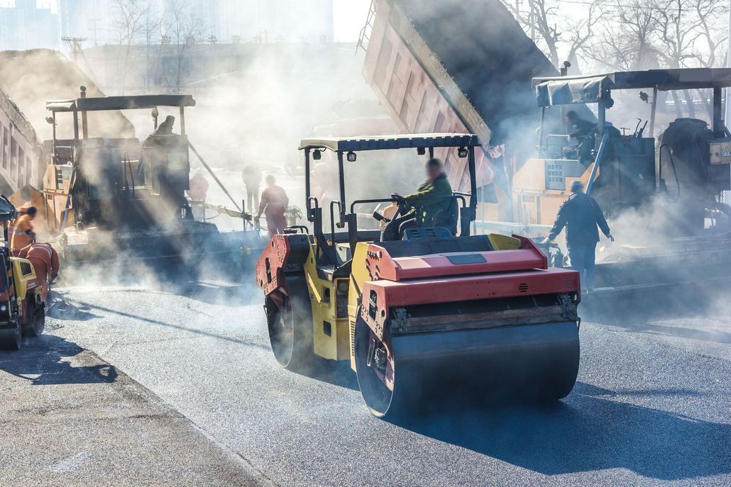 Steam rollers paving a road in a smoky construction site.