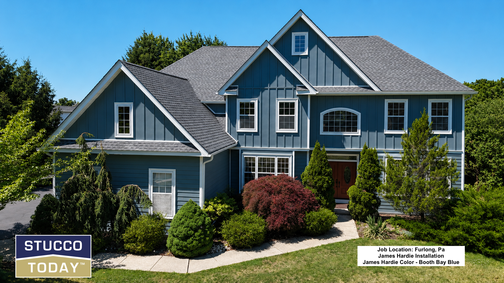Blue two-story stucco house with gray roof, front porch, and landscaped yard under a clear sky