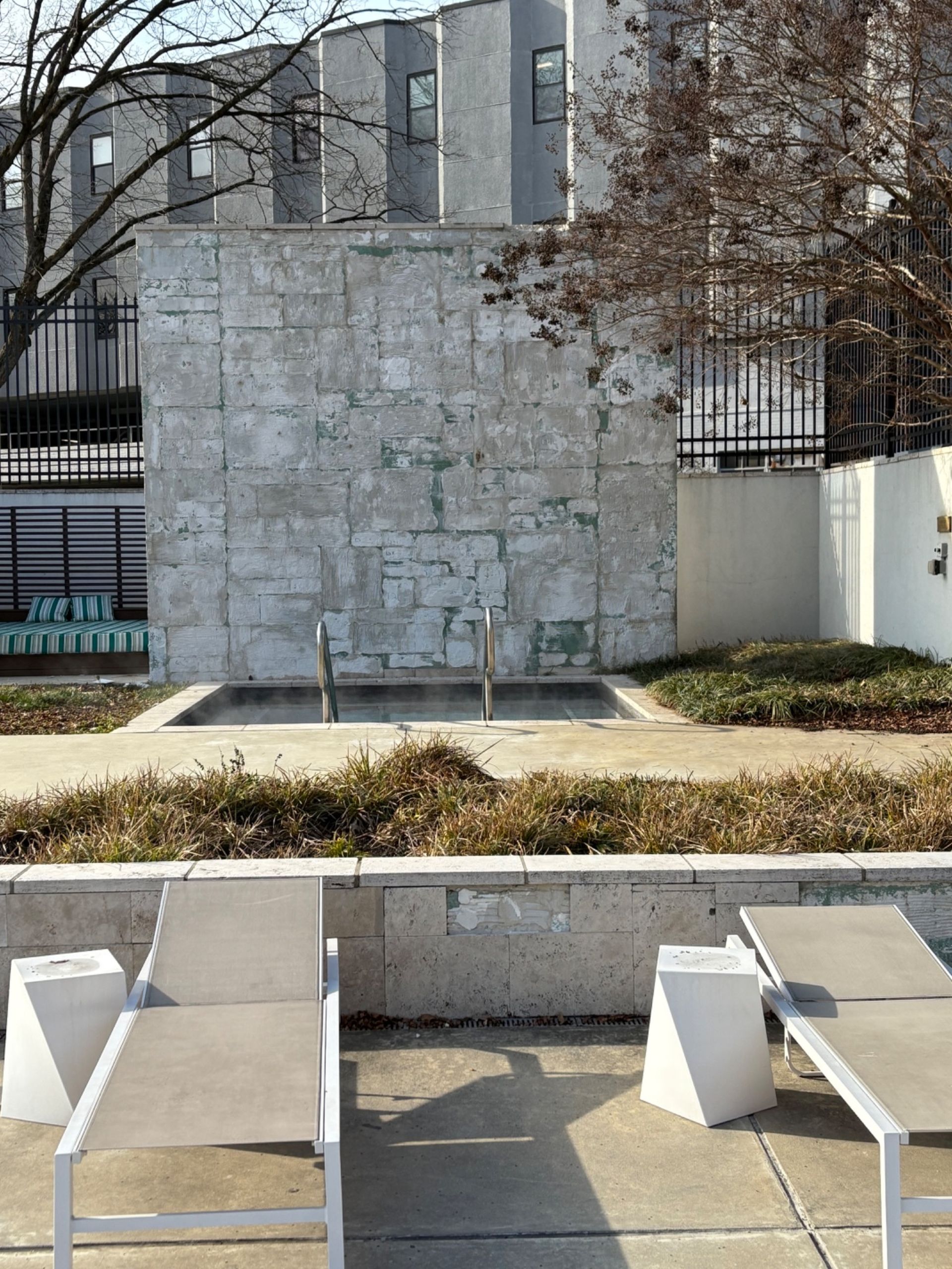 Poolside with lounge chairs facing a small water feature and textured stone wall.