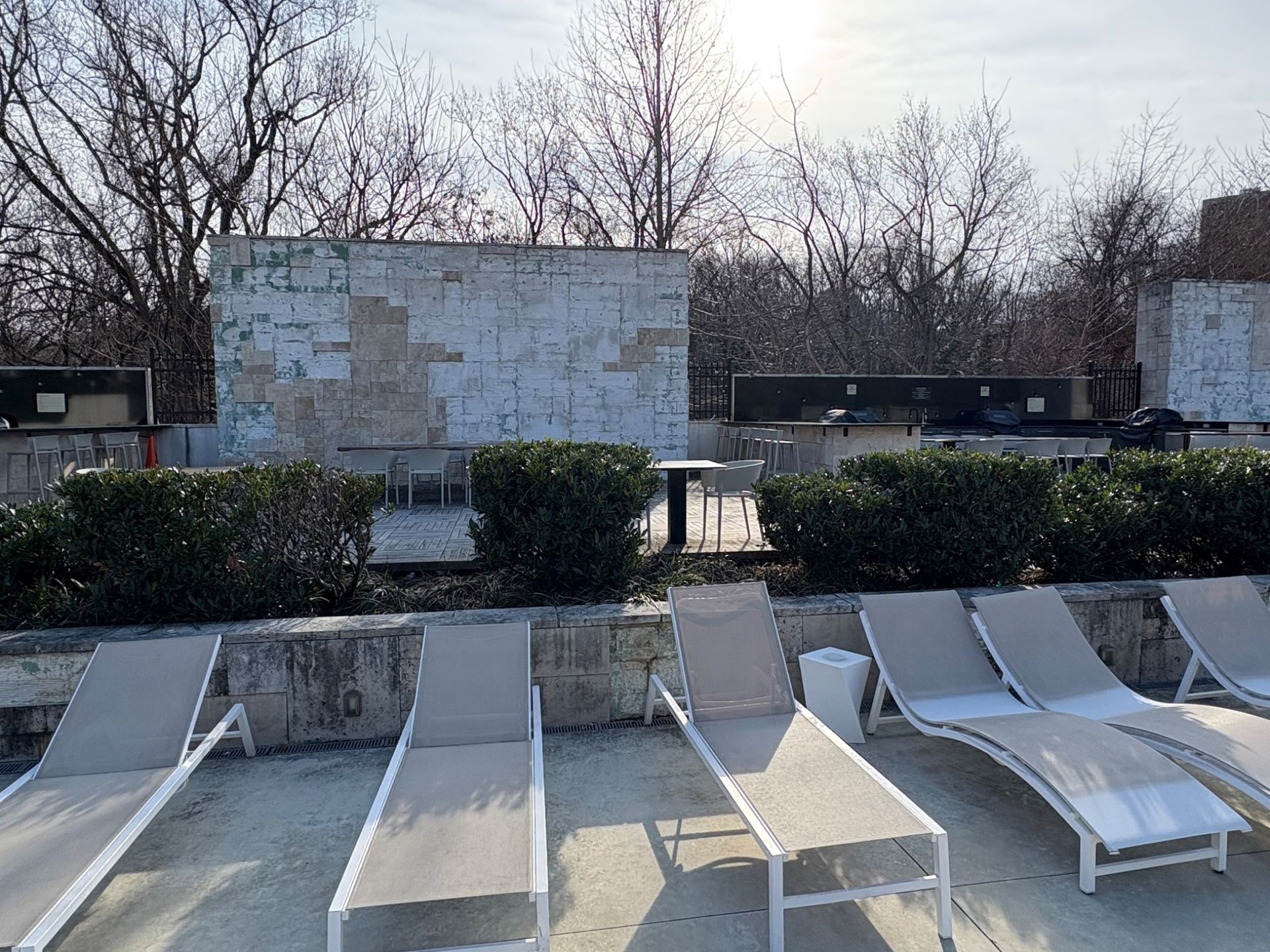 Lounge chairs on a rooftop patio; brick wall with peeling paint, bare trees in background.