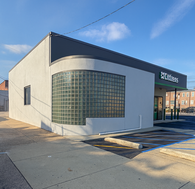 Citizens bank building with grey walls, curved corner, glass block window, and dark trim.