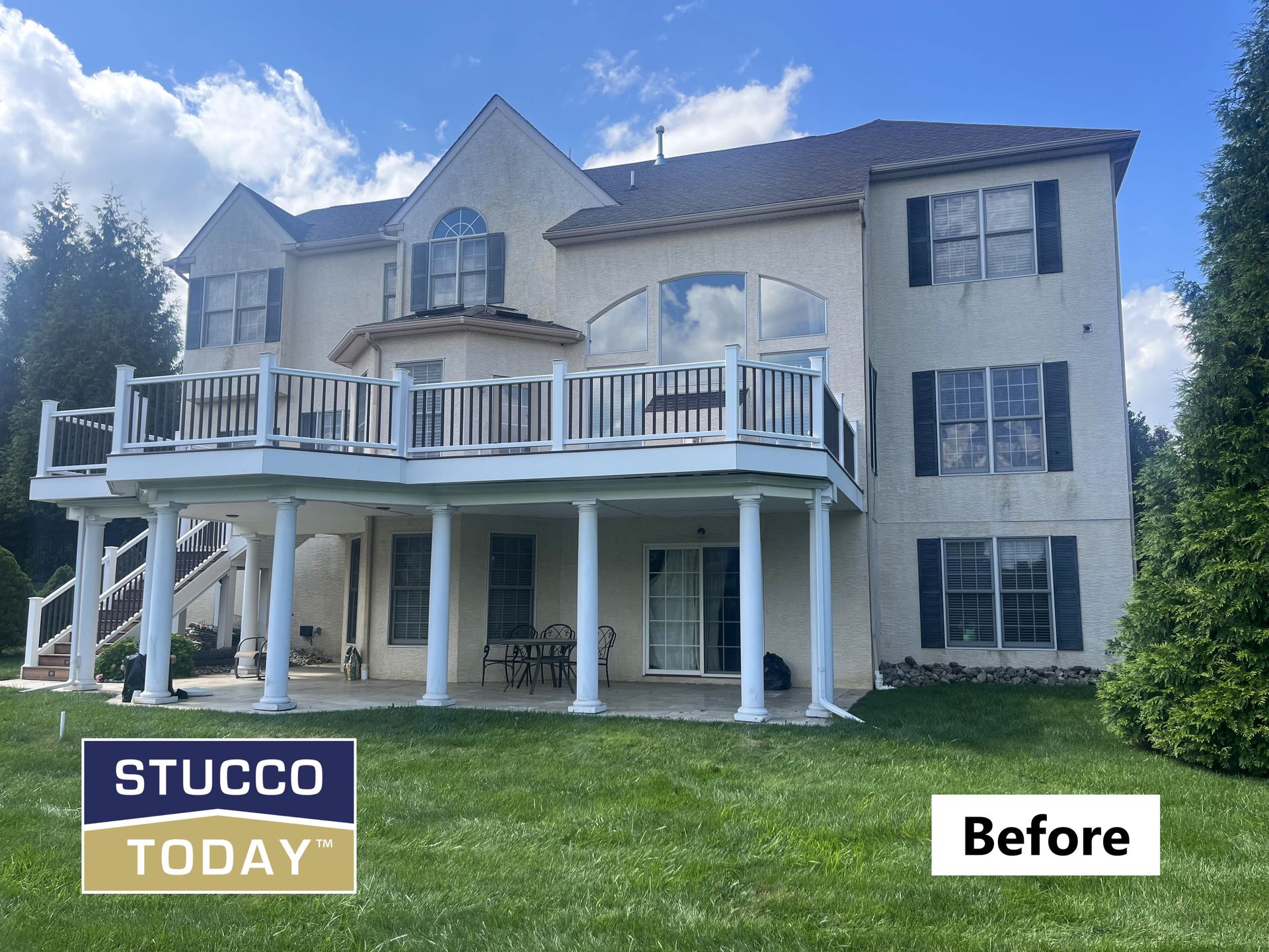 Back of a two-story beige stucco house with a deck, columns, windows, and green lawn, labeled 
