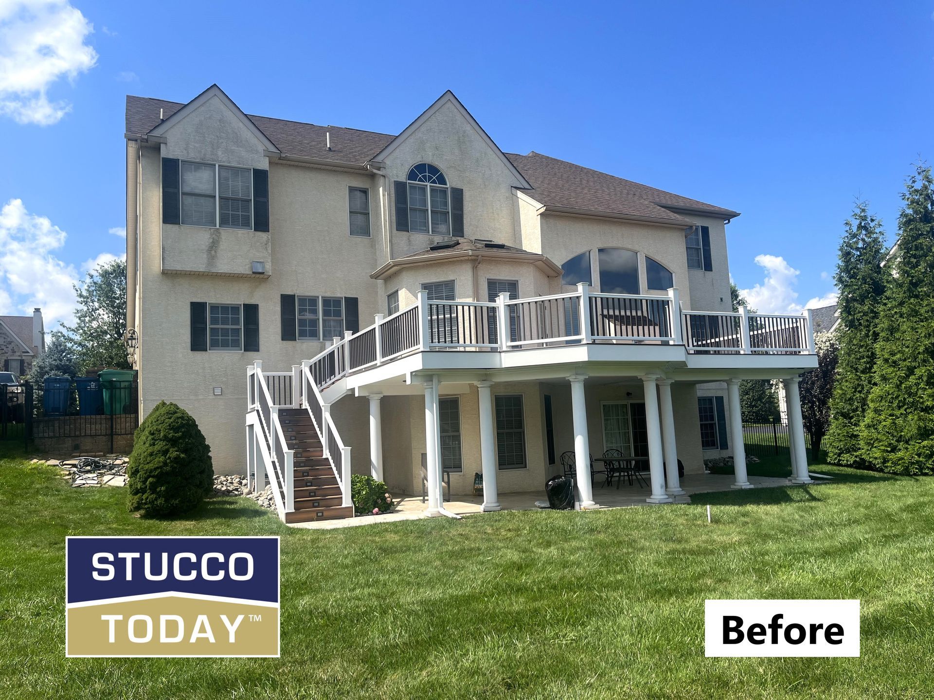 Back of a house with two-level deck, stucco exterior, and green lawn under blue sky. 