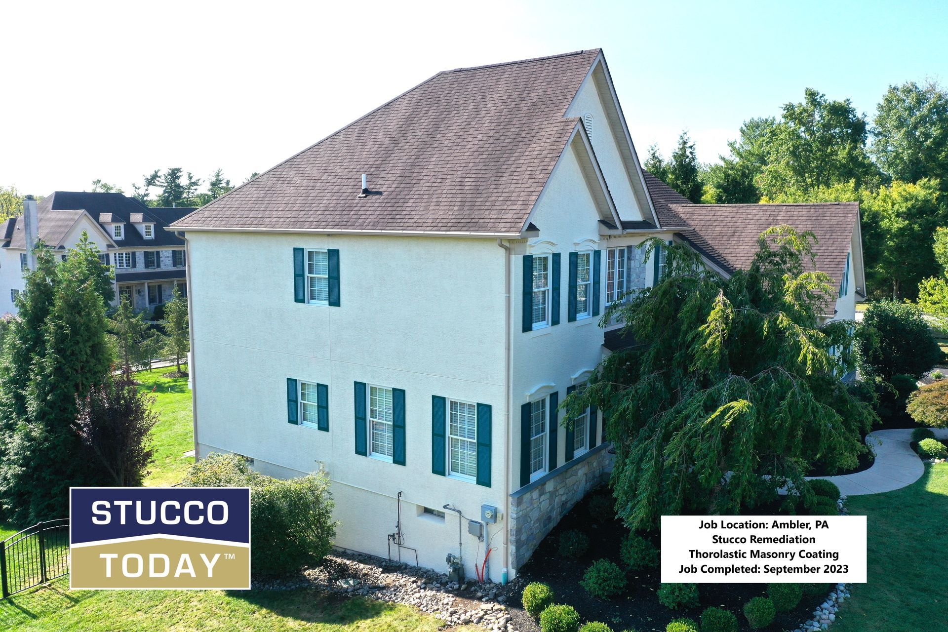 Two-story beige stucco house with green shutters and brown roof in a grassy yard.
