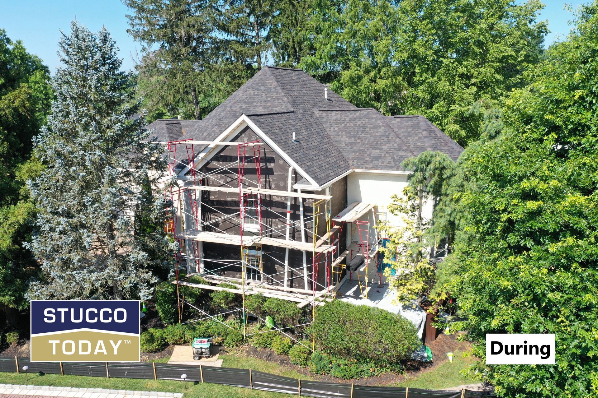 House during stucco installation, scaffolding, and mesh visible. Trees surround the building.