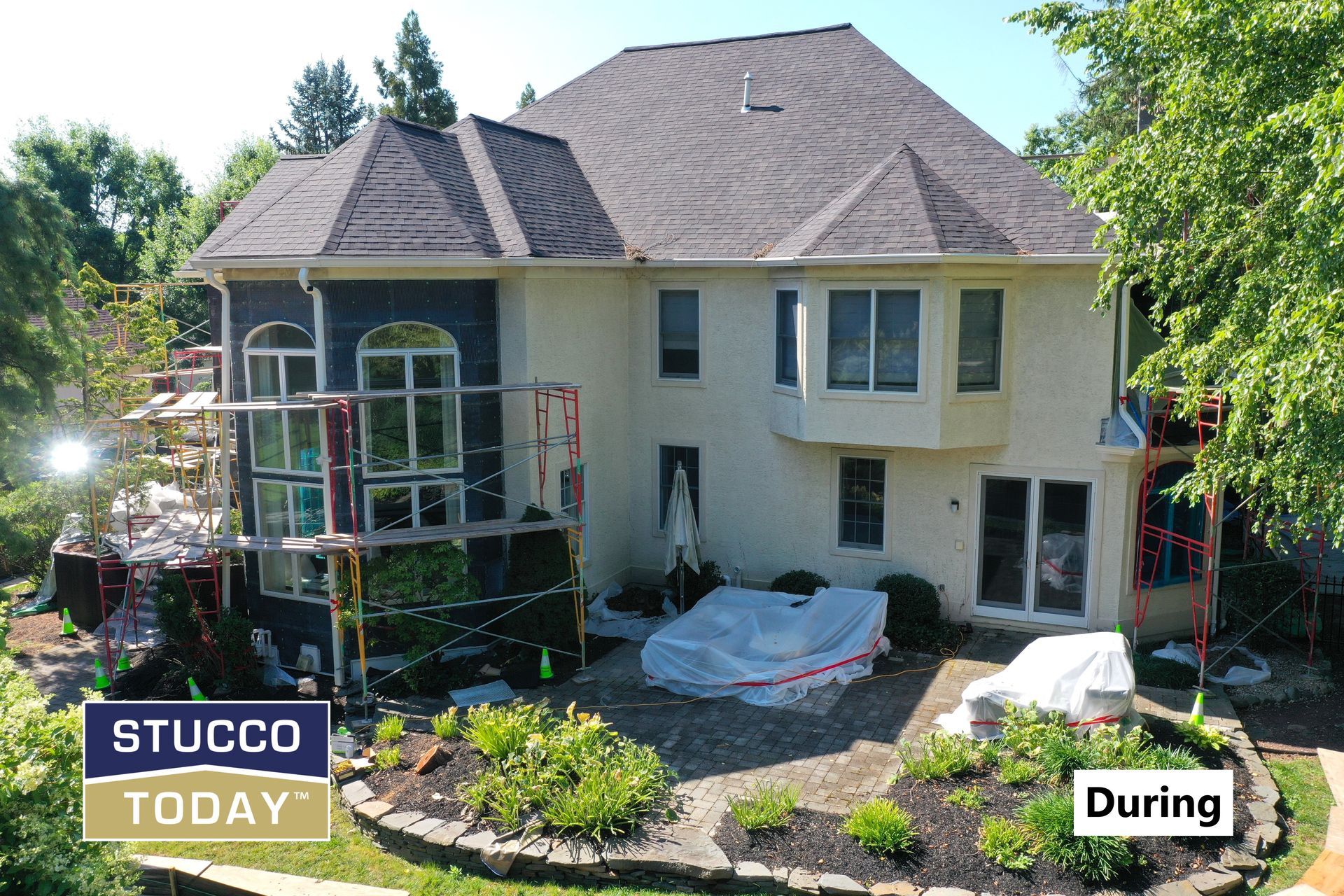 House undergoing stucco work; scaffolding, covered patio furniture, tan and dark stucco, during construction.