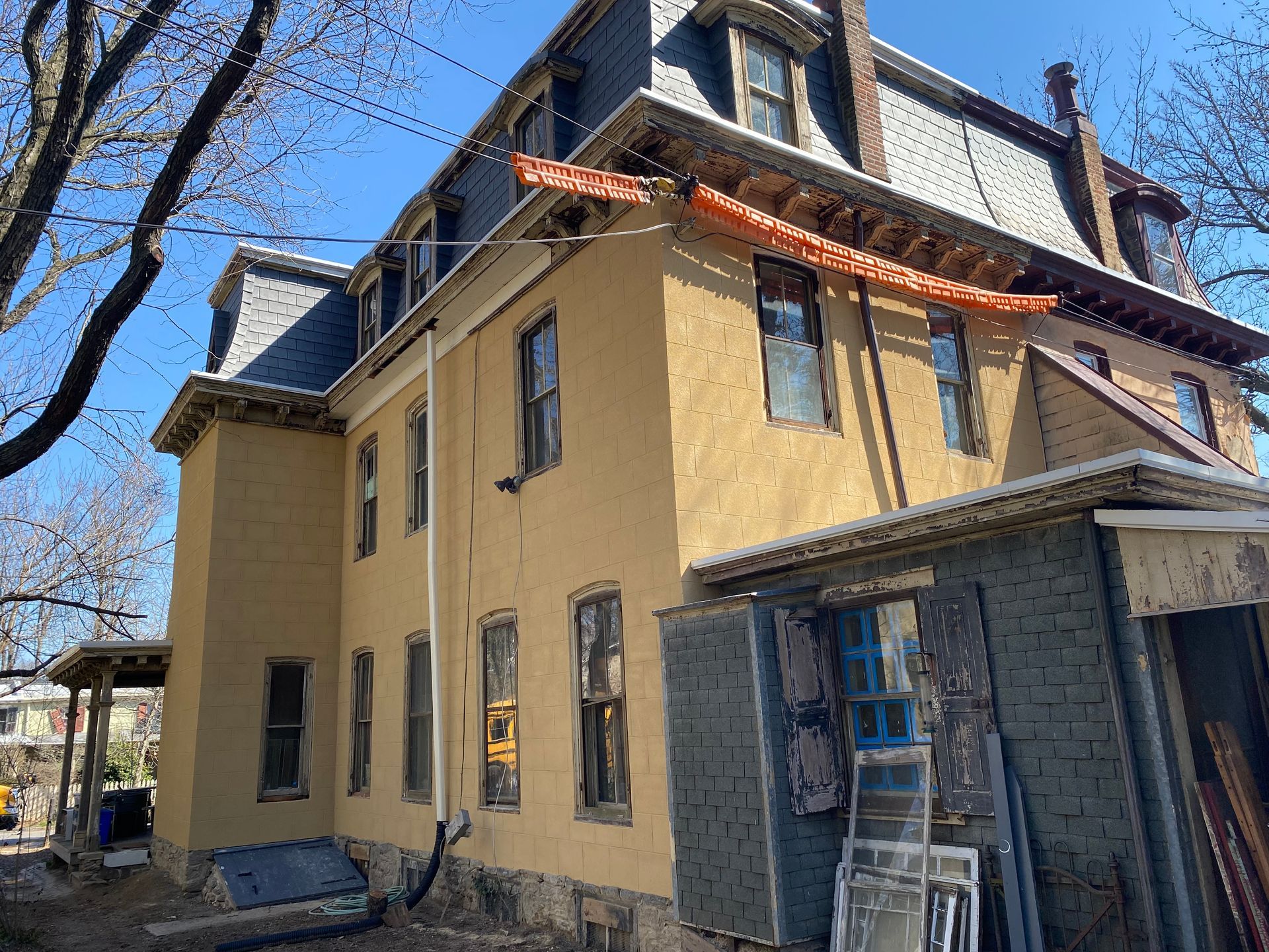 Yellow stucco house with dark roof, scaffolding, and open windows.