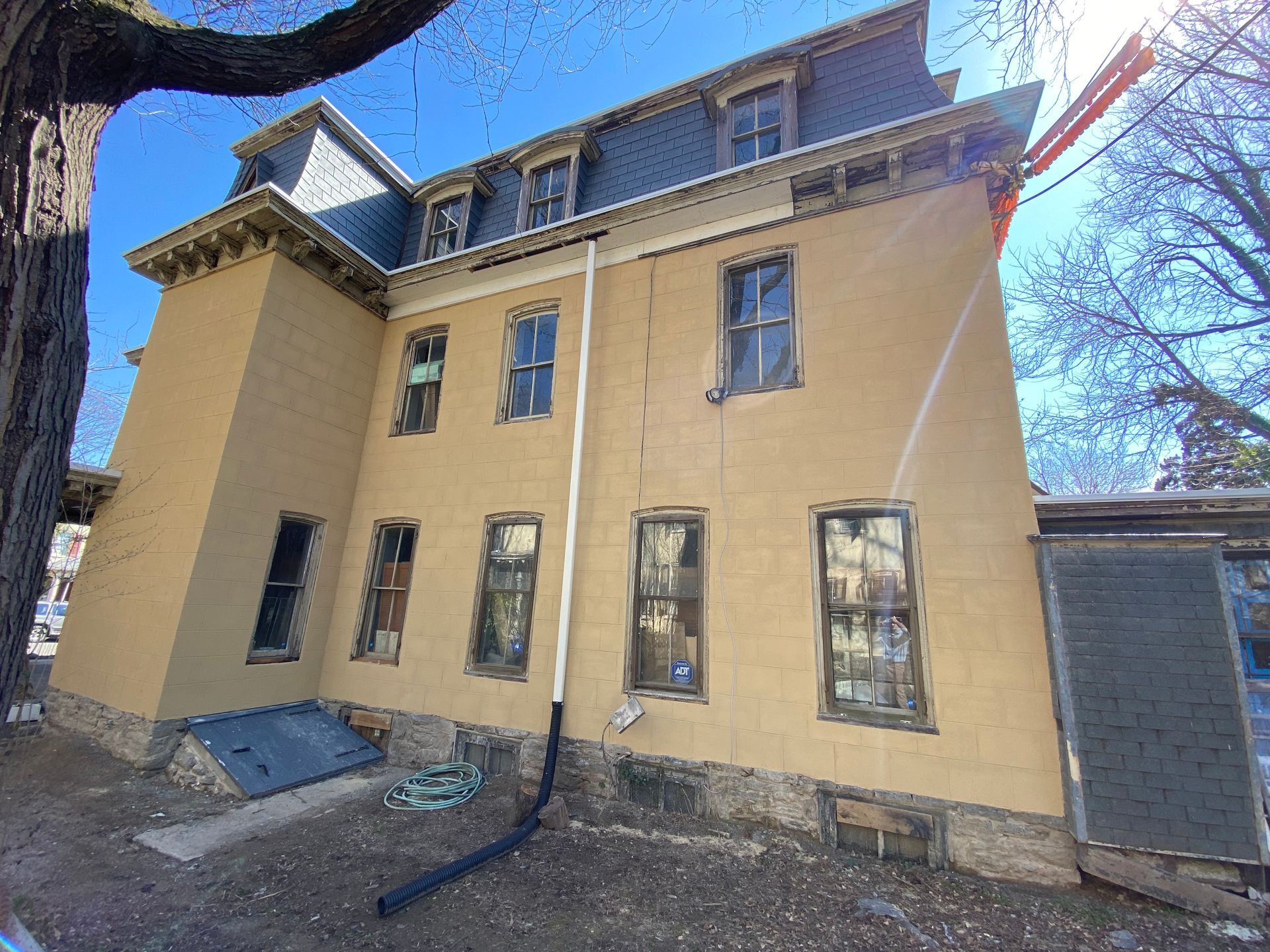 Tan, multi-story building with a dark gray roof and multiple windows. The side of the house is visible.