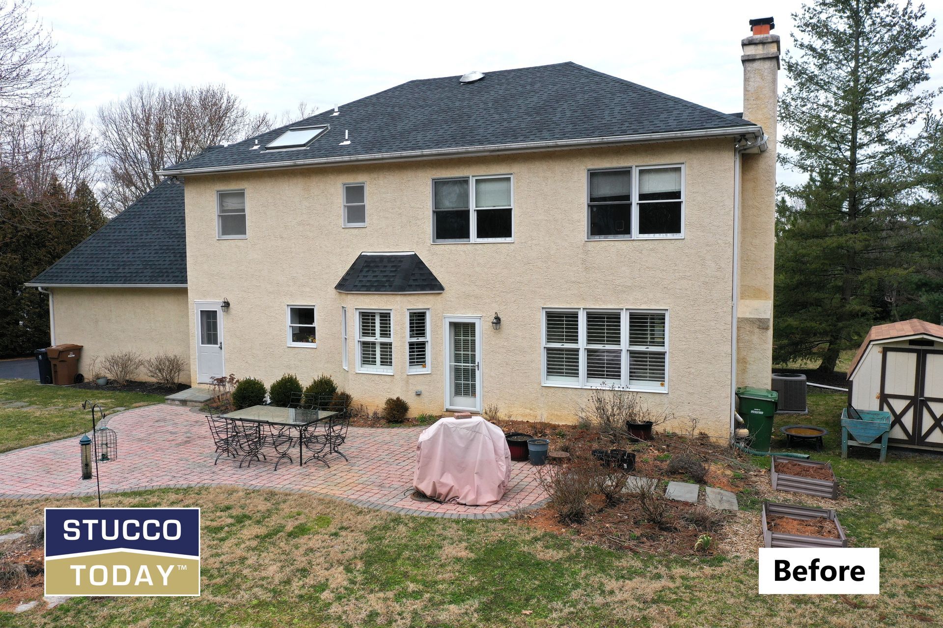 Back of a beige stucco house with dark roof and brick patio; 