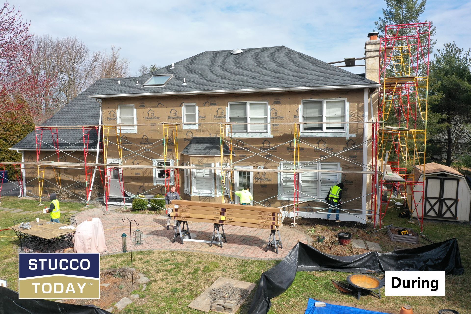 Stucco being applied to a two-story house, workers on scaffolding.