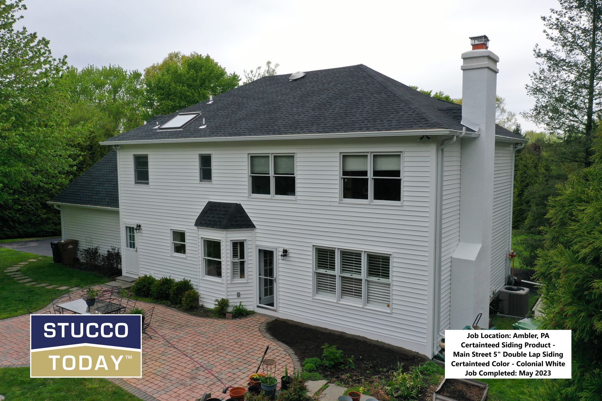 White house with a dark roof and brick patio. Text: Stucco Today.