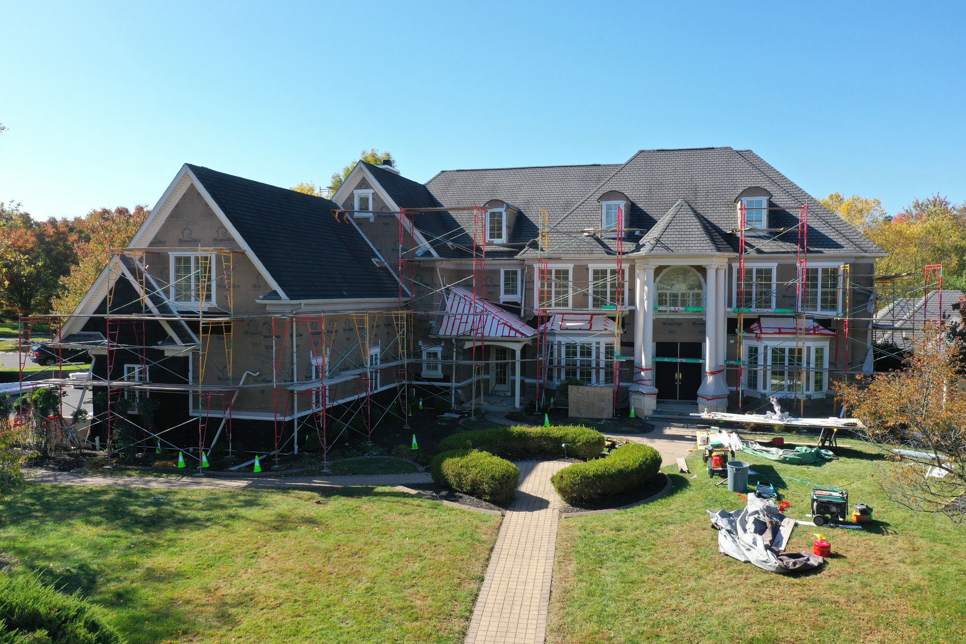 House under construction with scaffolding, workers, and tools on a sunny day.