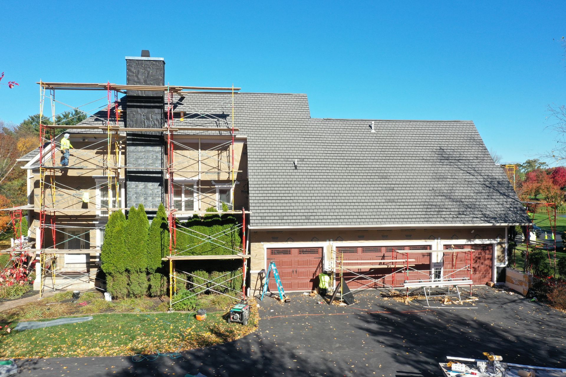 House with scaffolding, workers, and a driveway undergoing construction on a sunny day.