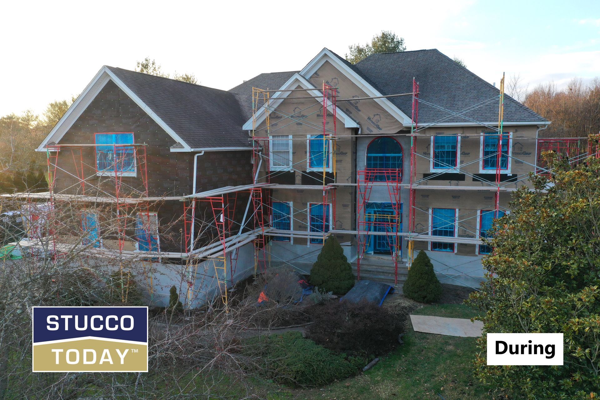 House under construction; scaffolding surrounds, blue windows, stucco process.