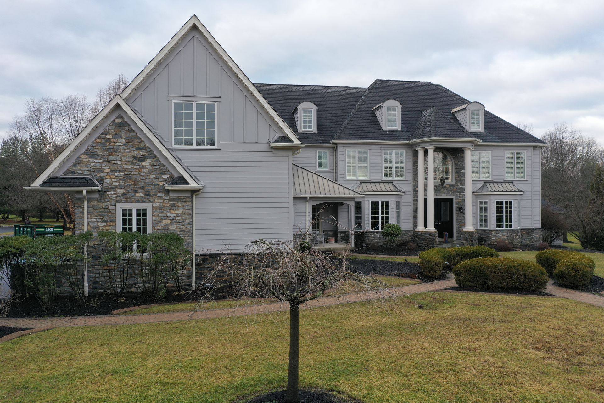 Large gray house with stone accents, columns, and a lawn on a cloudy day.