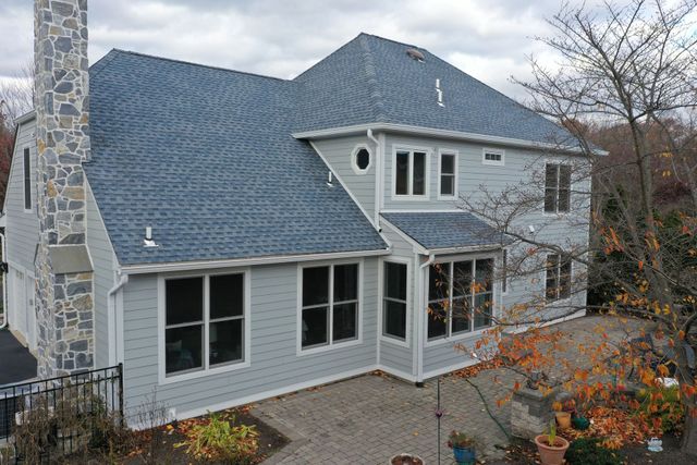 Two-story house with gray siding and roof. Stone chimney. Windows and a patio are visible.