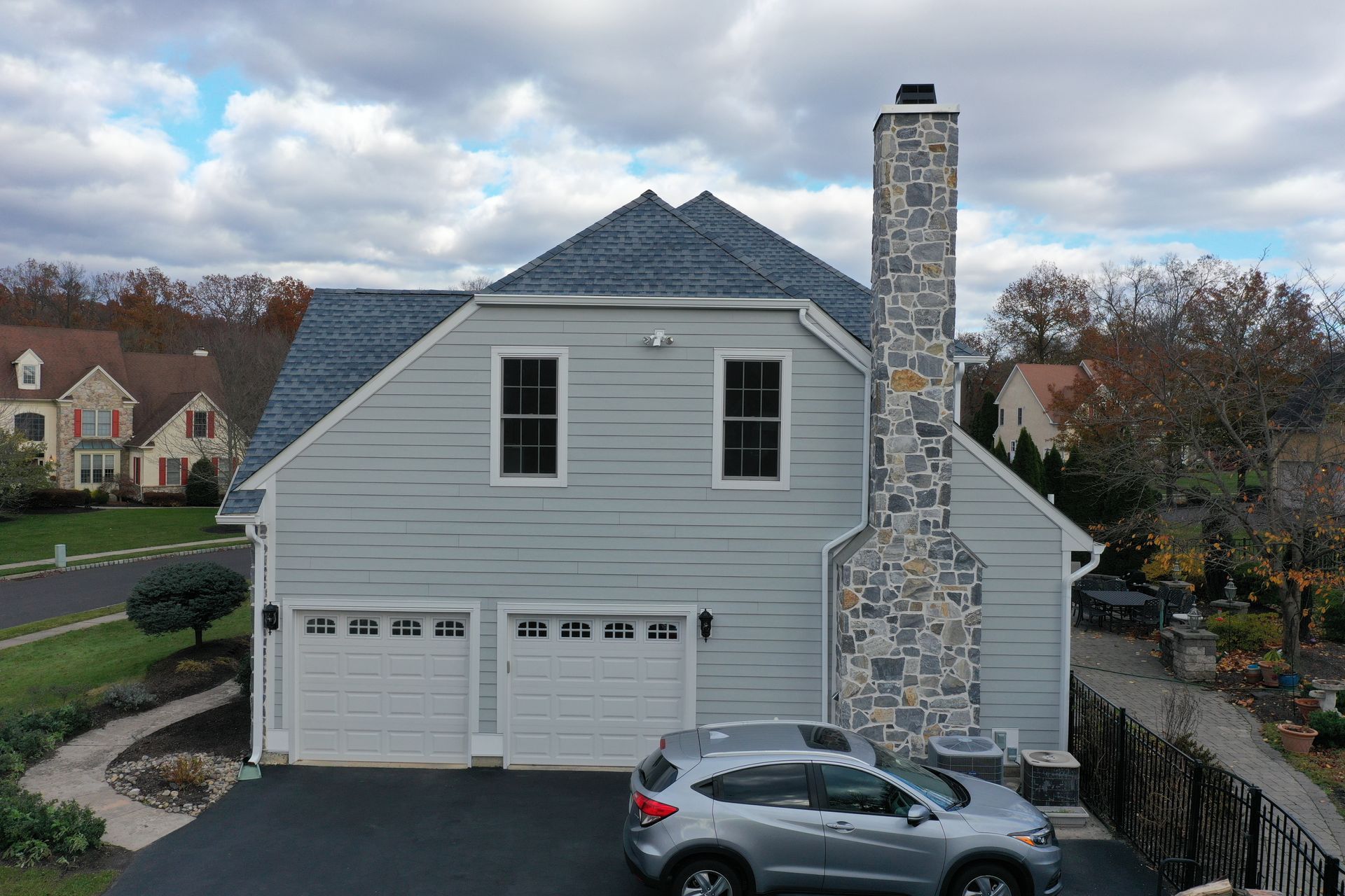 A two-car garage with a stone chimney, blue-gray siding, and a silver car parked in the driveway.