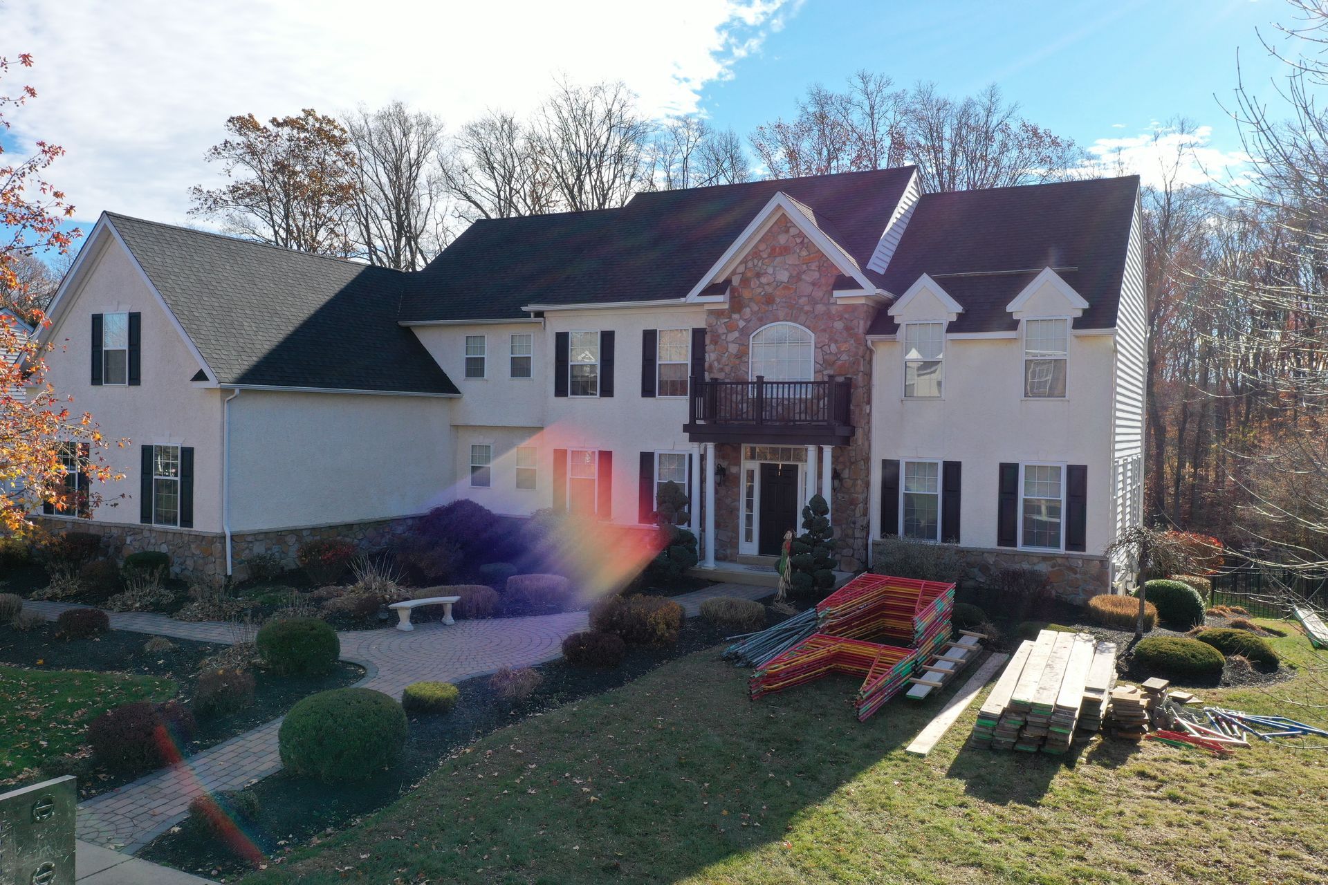 Two-story house with dark roof and tan siding.  Stone accent on front. Building materials on lawn.