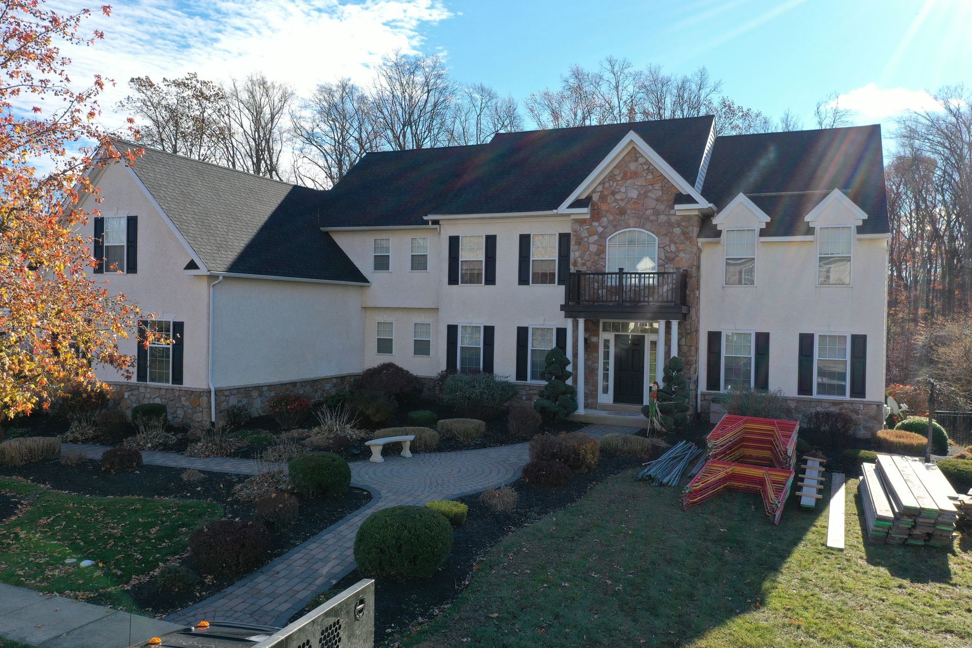 Large two-story house with black shutters, stone accents, and a landscaped front yard with a walkway.