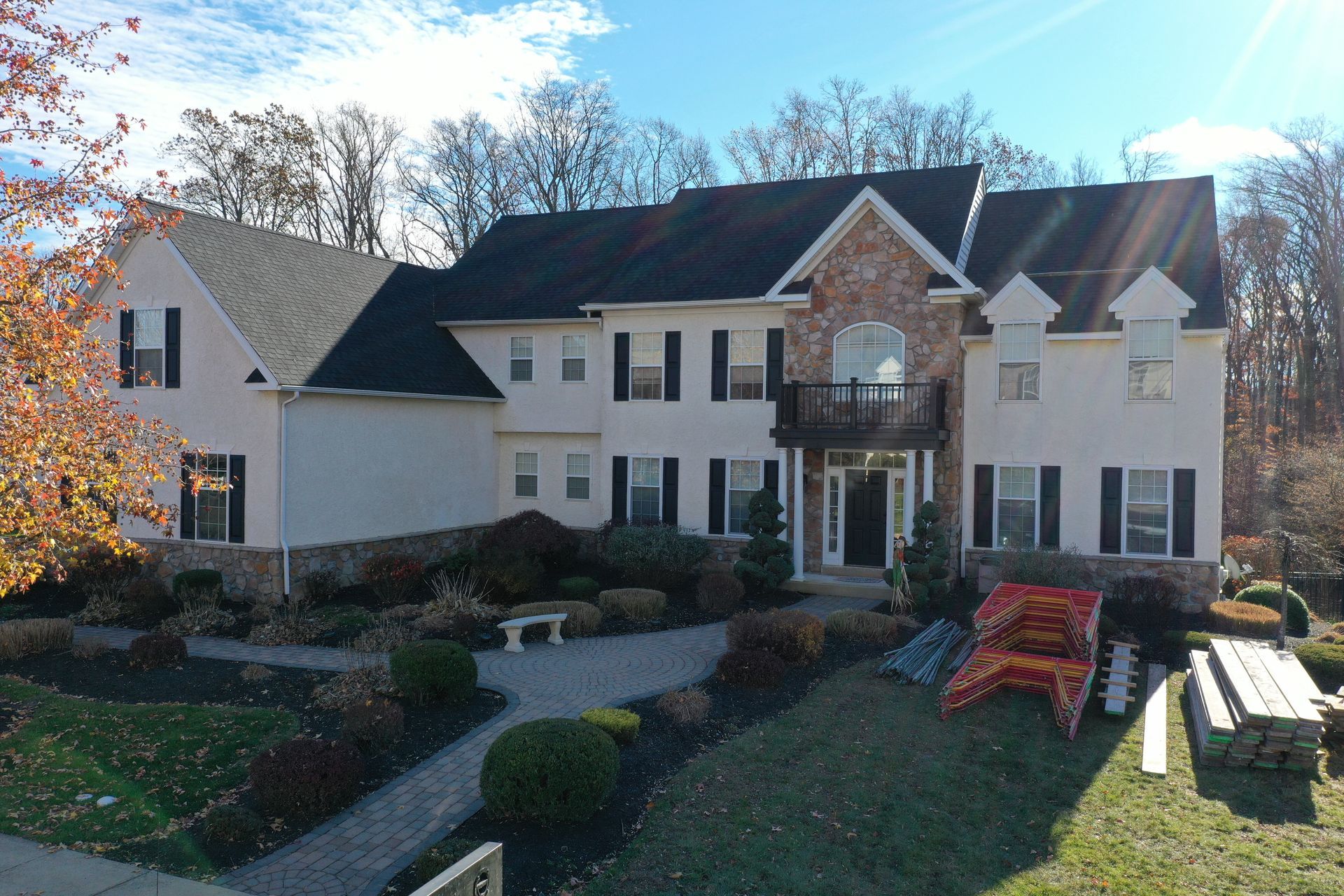 Large beige house with black shutters, stone accents, and a black roof on a sunny day.