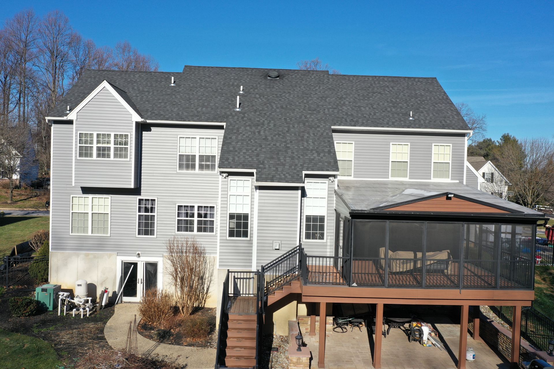 Two-story gray house with a dark roof and a screened porch, surrounded by a deck and a yard.