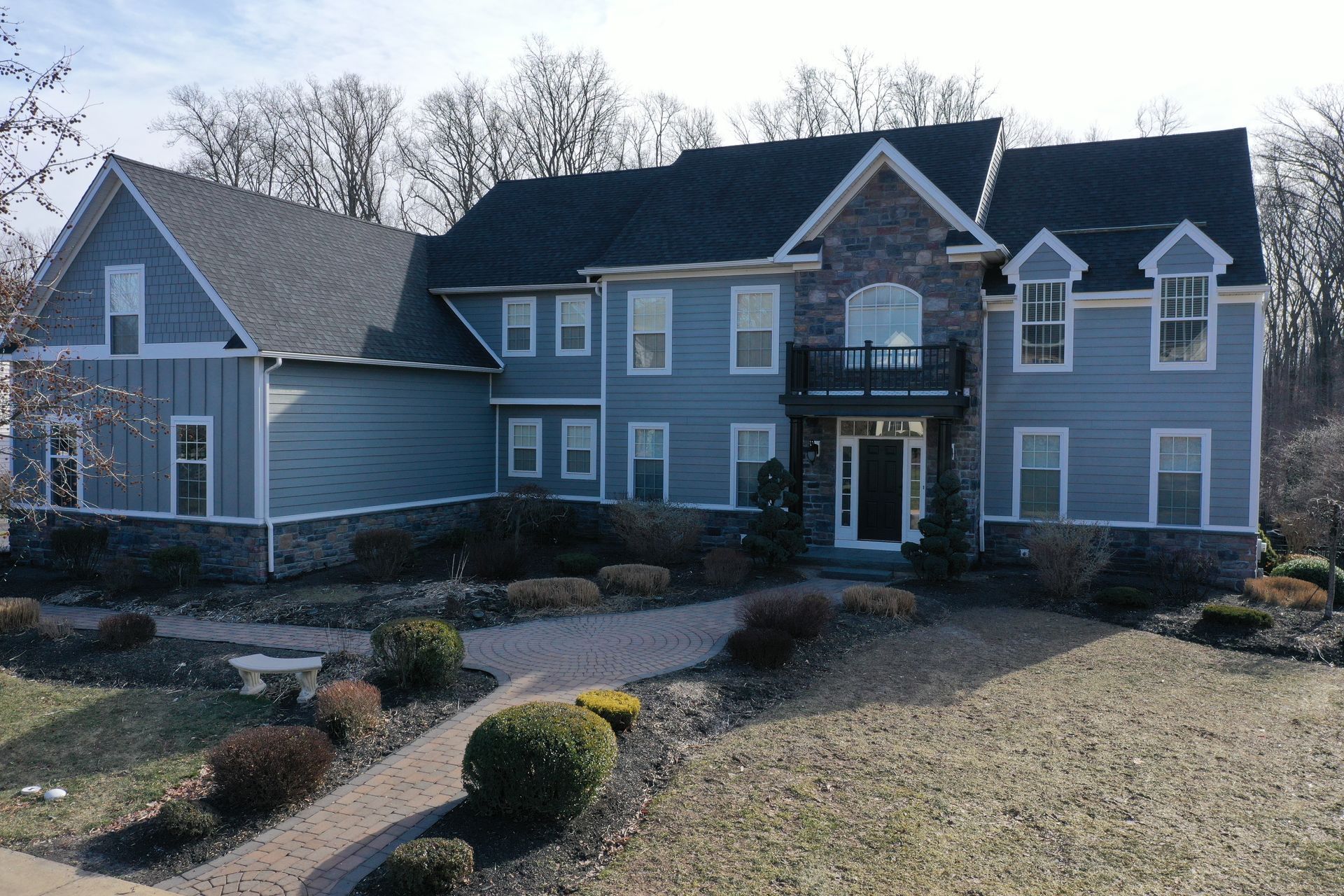 Two-story blue house with stone accents, black roof, and manicured landscaping in a yard.