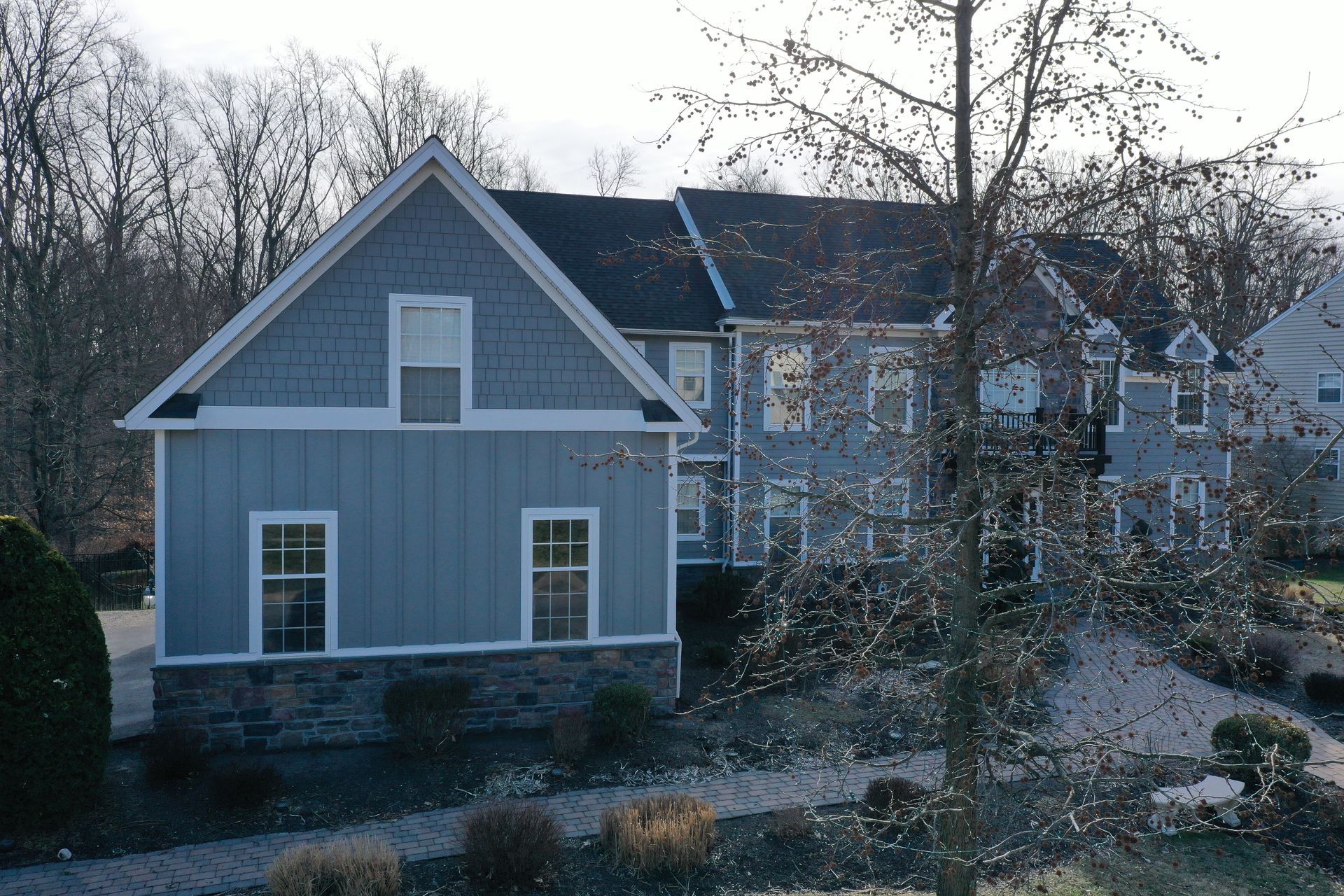 Blue and grey house with stone base and many windows; trees in the background.