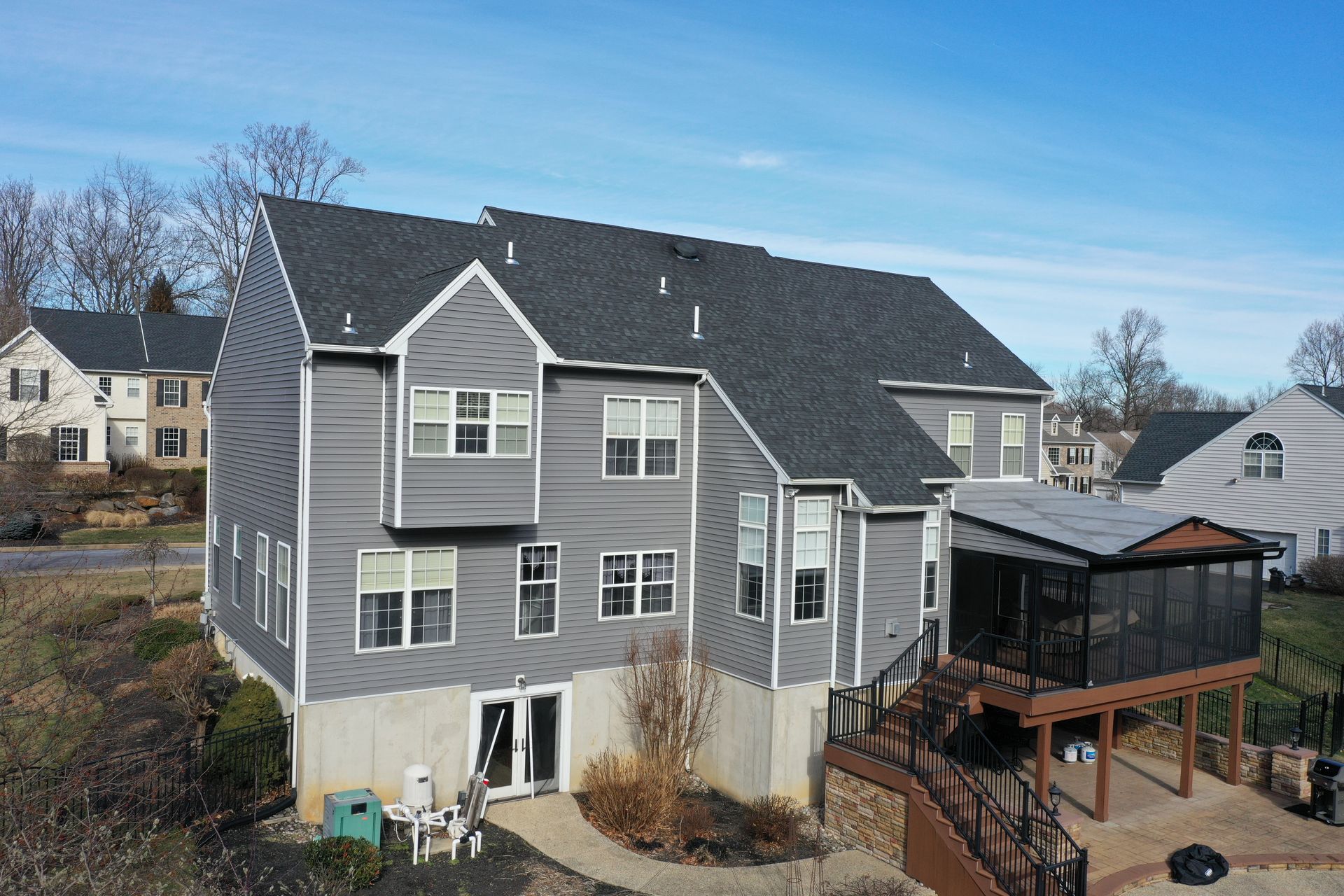 Two-story gray house with dark roof and screened porch; sunny day.