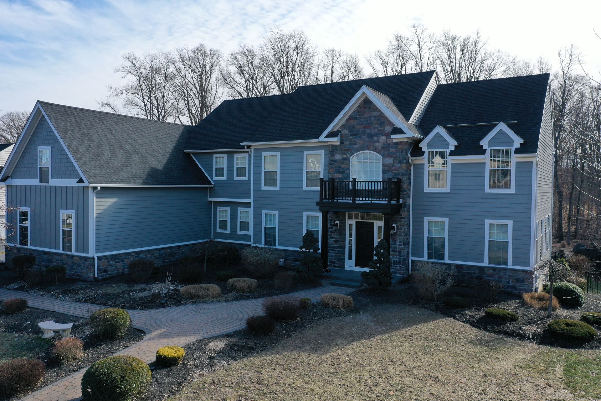 Two-story blue house with stone accents, a dark roof, and small front yard with shrubs.