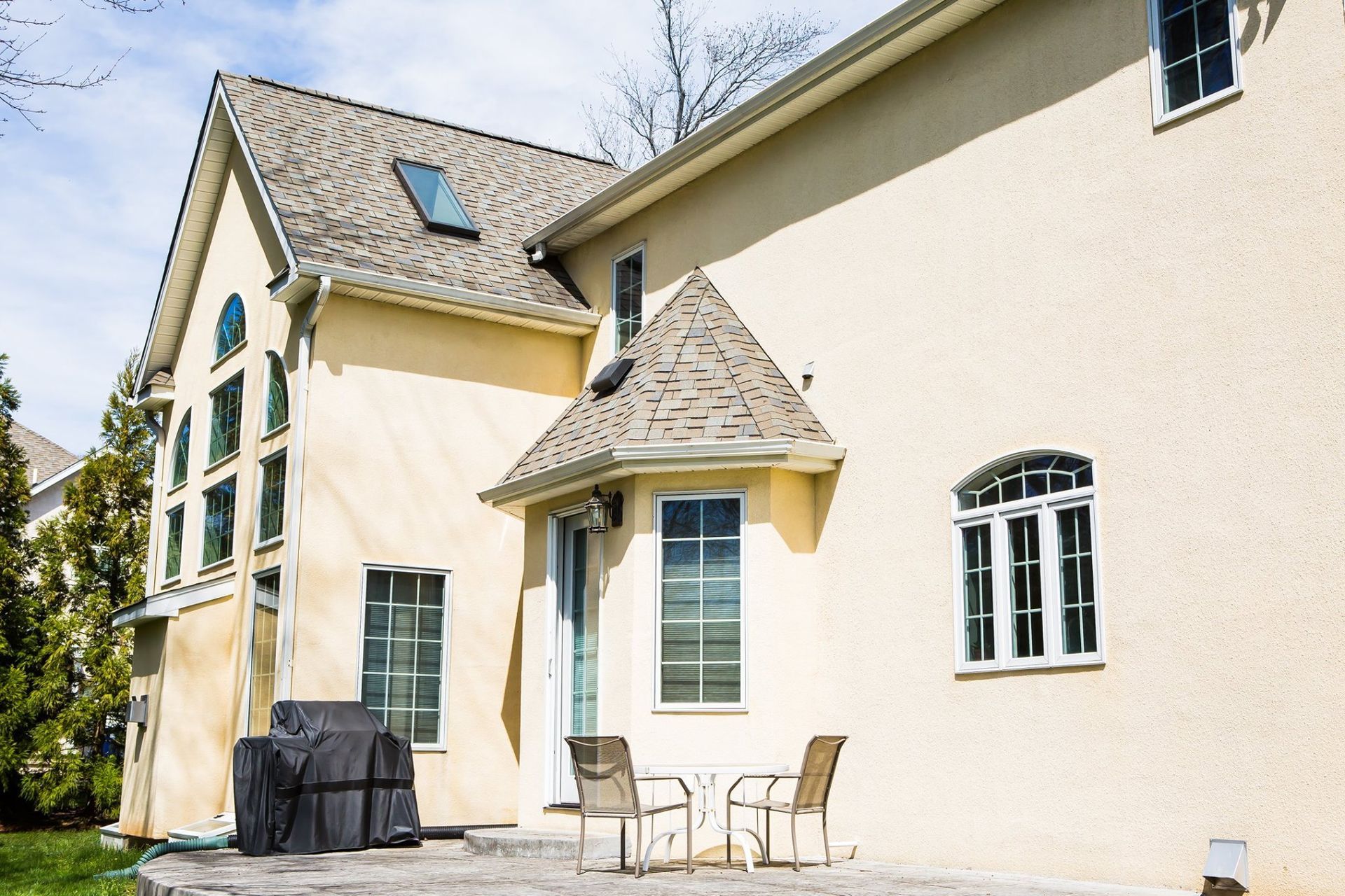 Beige house exterior with multiple windows and a small patio, under a blue sky.