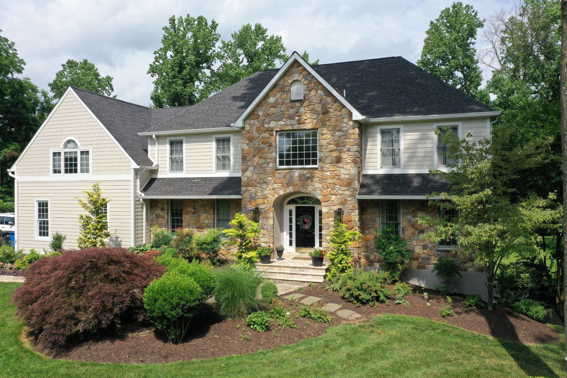 House with stone facade and beige siding, surrounded by landscaping and trees.