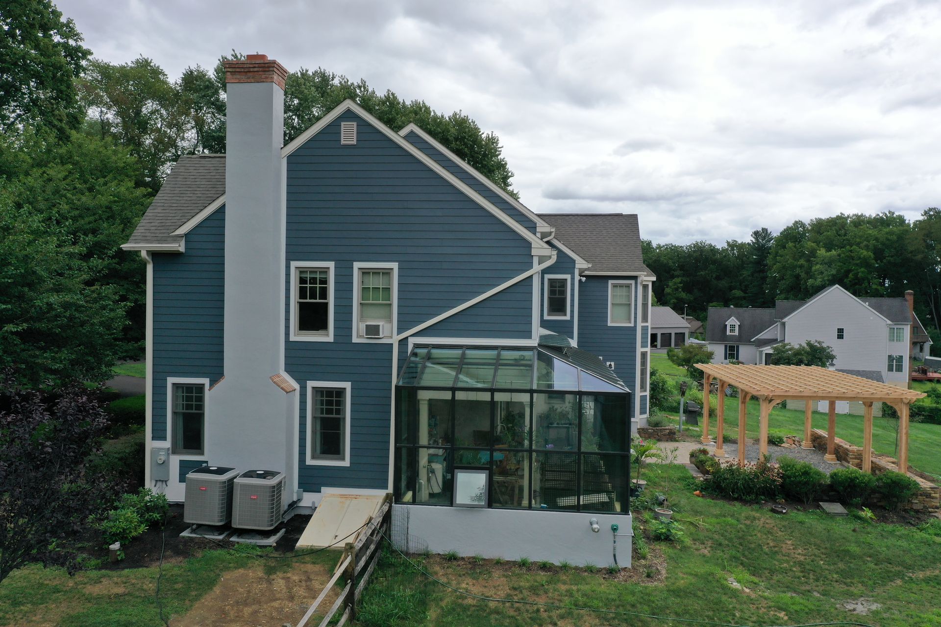 Blue house with a glass sunroom, white chimney, and pergola in a yard.