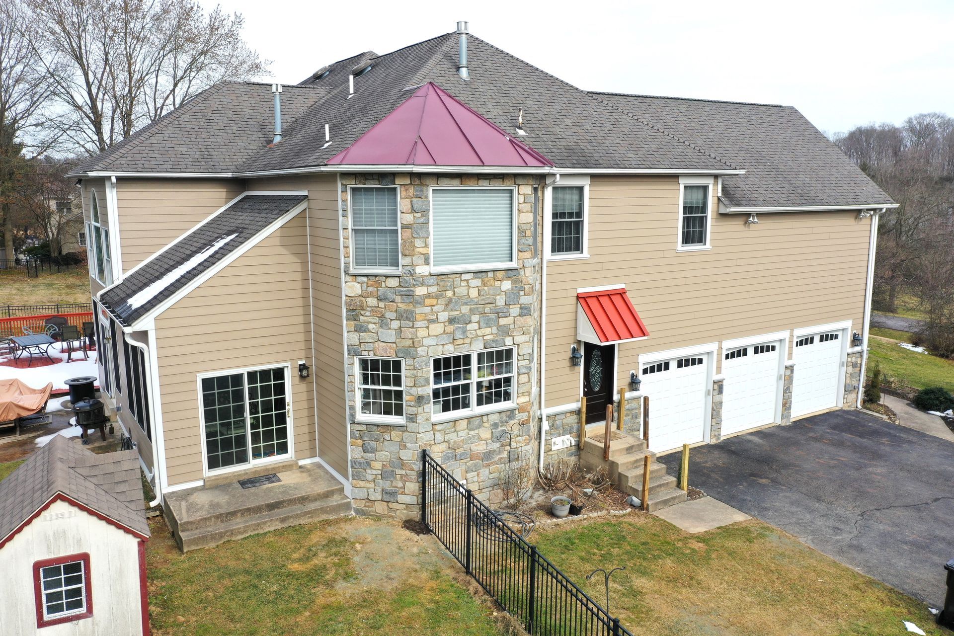 Two-story beige house with stone facade, red accents, and a three-car garage.