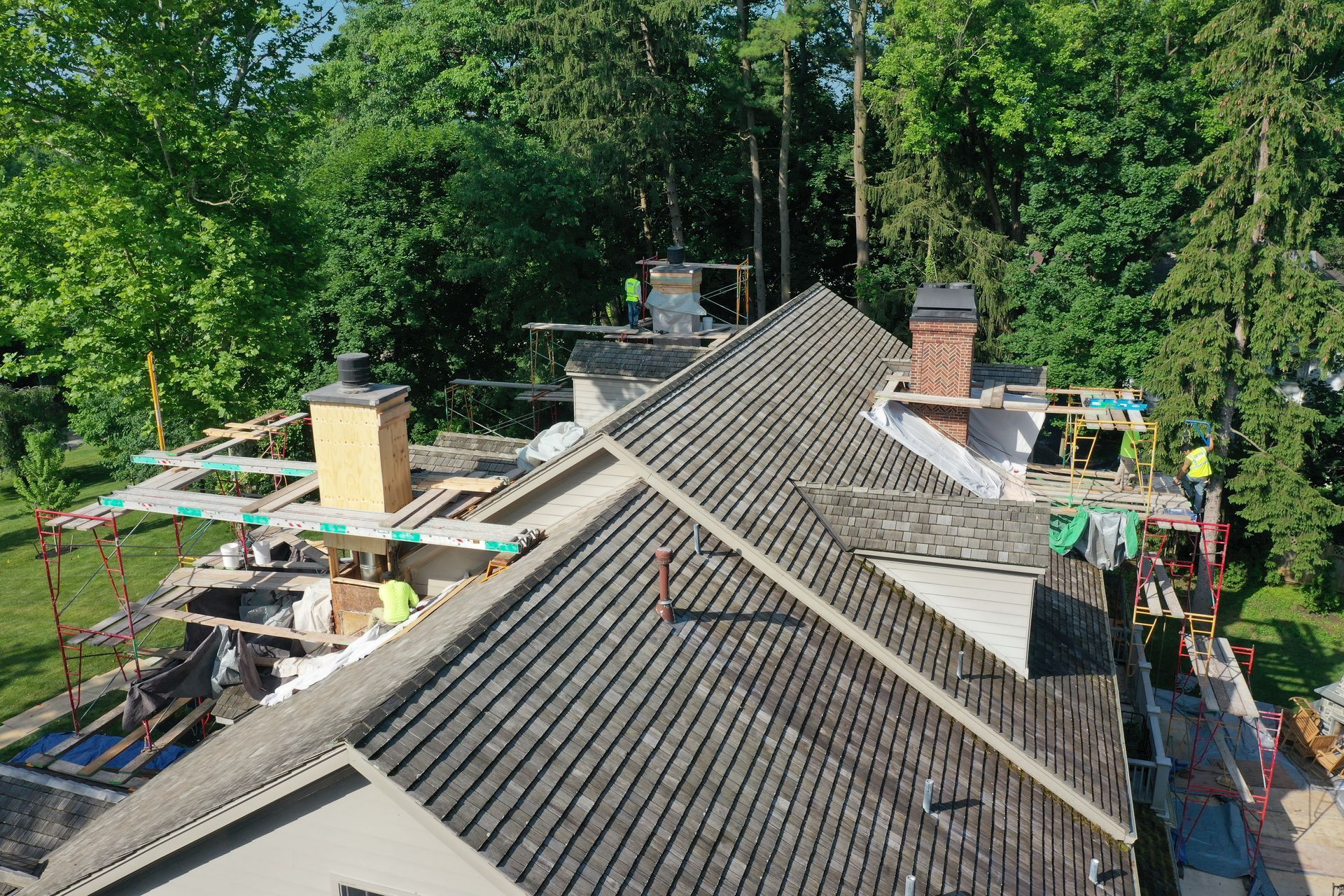 Roof of a house under construction; workers on scaffolding; trees in background.